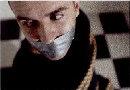 A man with tape over his mouth and a rope around his neck, looking frightened.