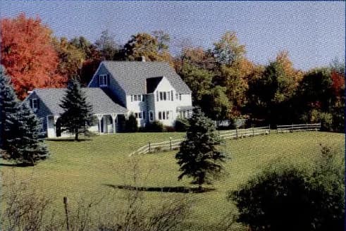 A large house with a garden and trees in autumn colours, in the countryside.
