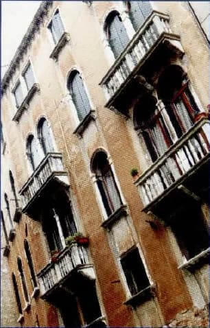 A tall old apartment building with balconies and shutters, in a city.