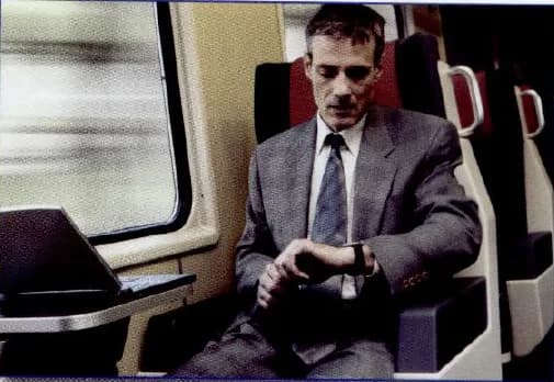 A businessman in a suit sitting on a train, looking at his watch.
