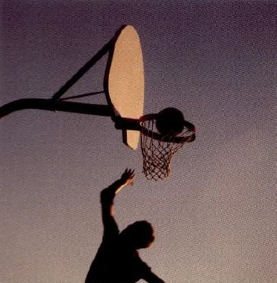 The silhouette of a basketball player jumping towards the hoop.