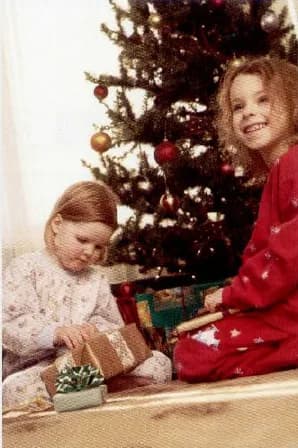 Two little girls opening presents next to a Christmas tree.