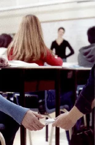 A classroom where one student secretly passes a piece of paper to another during a test.