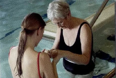 An older woman helping a girl with an exercise in a swimming pool.