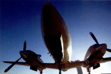 A small twin-engine aeroplane seen from below against a blue sky.